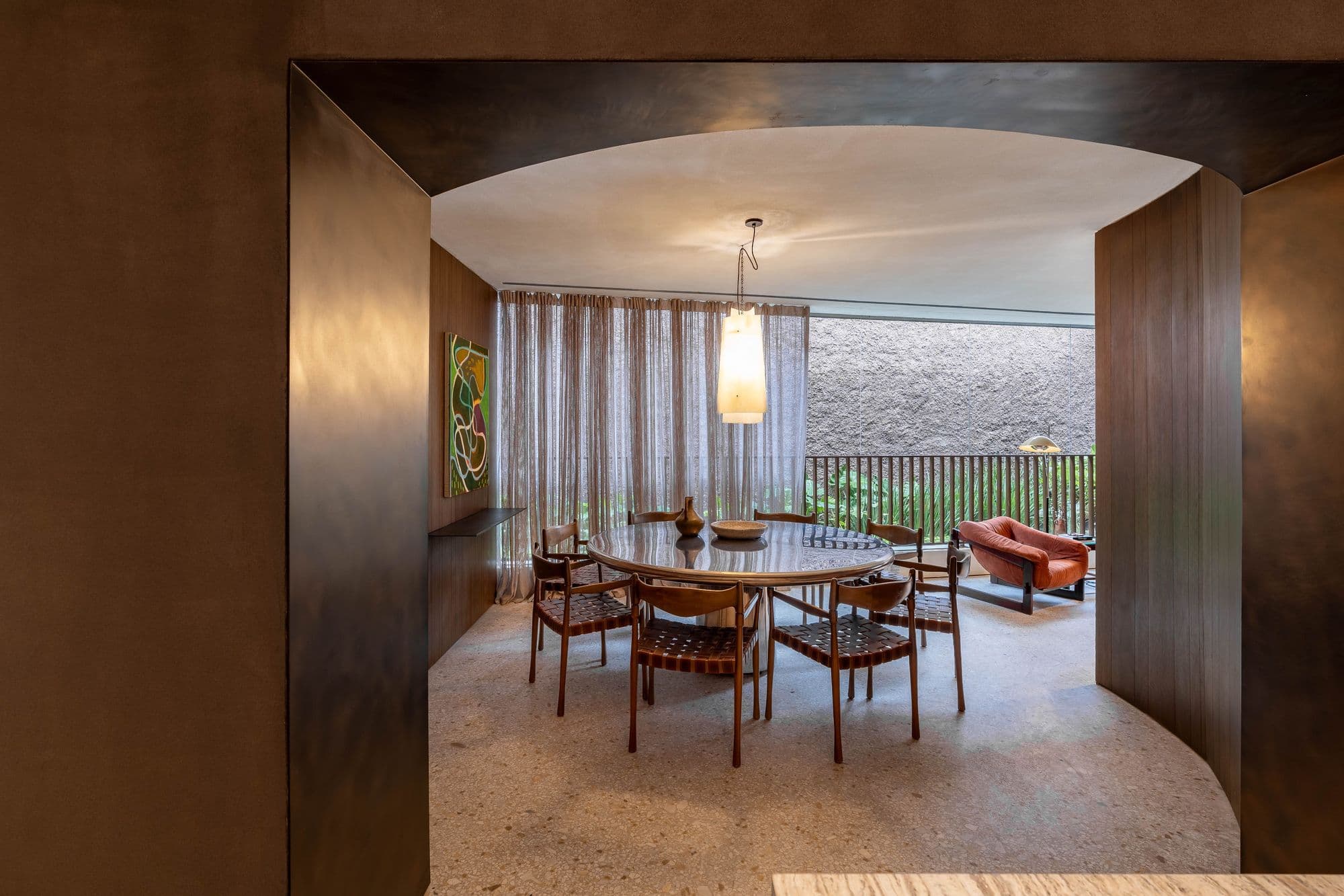 Portal curvo em madeira escura que emoldura a sala de jantar