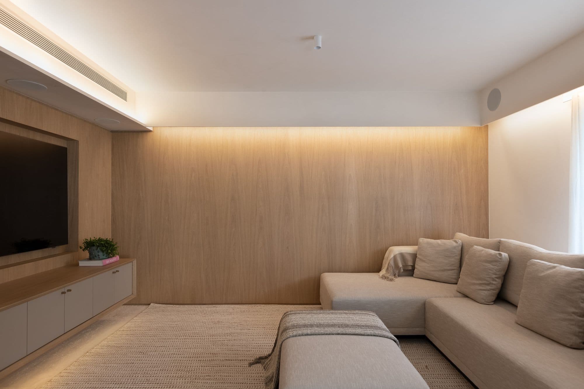 Sala de TV revestida em madeira clara com sanca iluminada
